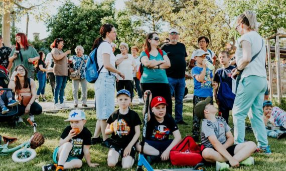 A diverse group of families and children enjoying an outdoor event on a sunny day in a park setting.