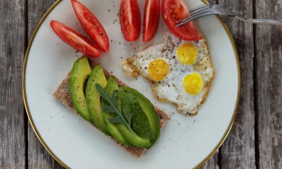 Delicious breakfast plate with sliced avocado, tomatoes, and sunny-side-up quail eggs.
