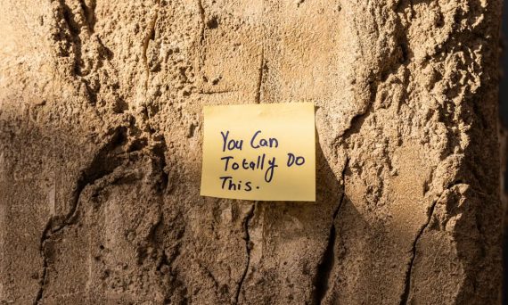 A sticky note with a motivational message on a textured wall in Dubai, with sunlight casting shadows.